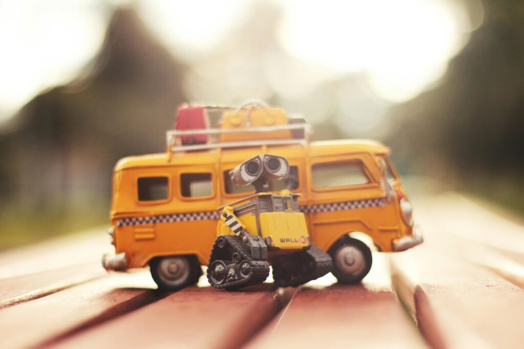 Charming miniature robot with yellow van toy in blurred outdoor daylight, capturing playful leisure theme.